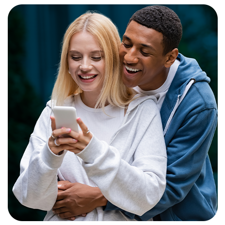 Casal sorrindo enquanto consulta informações em um celular.