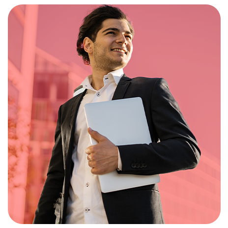 Jovem, sorrindo, de paletó preto e camisa branca, sem gravata, segurando um notebook embaixo do braço.