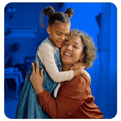 Mulher e criança se abraçando com carinho, sorrindo, em ambiente interno com fundo azul.