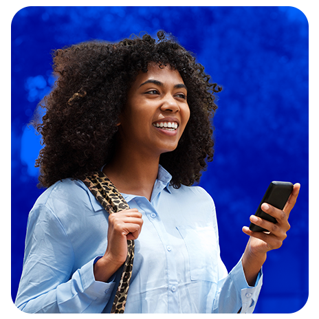 Mulher sorrindo segurando celular, com bolsa no ombro e fundo azul.