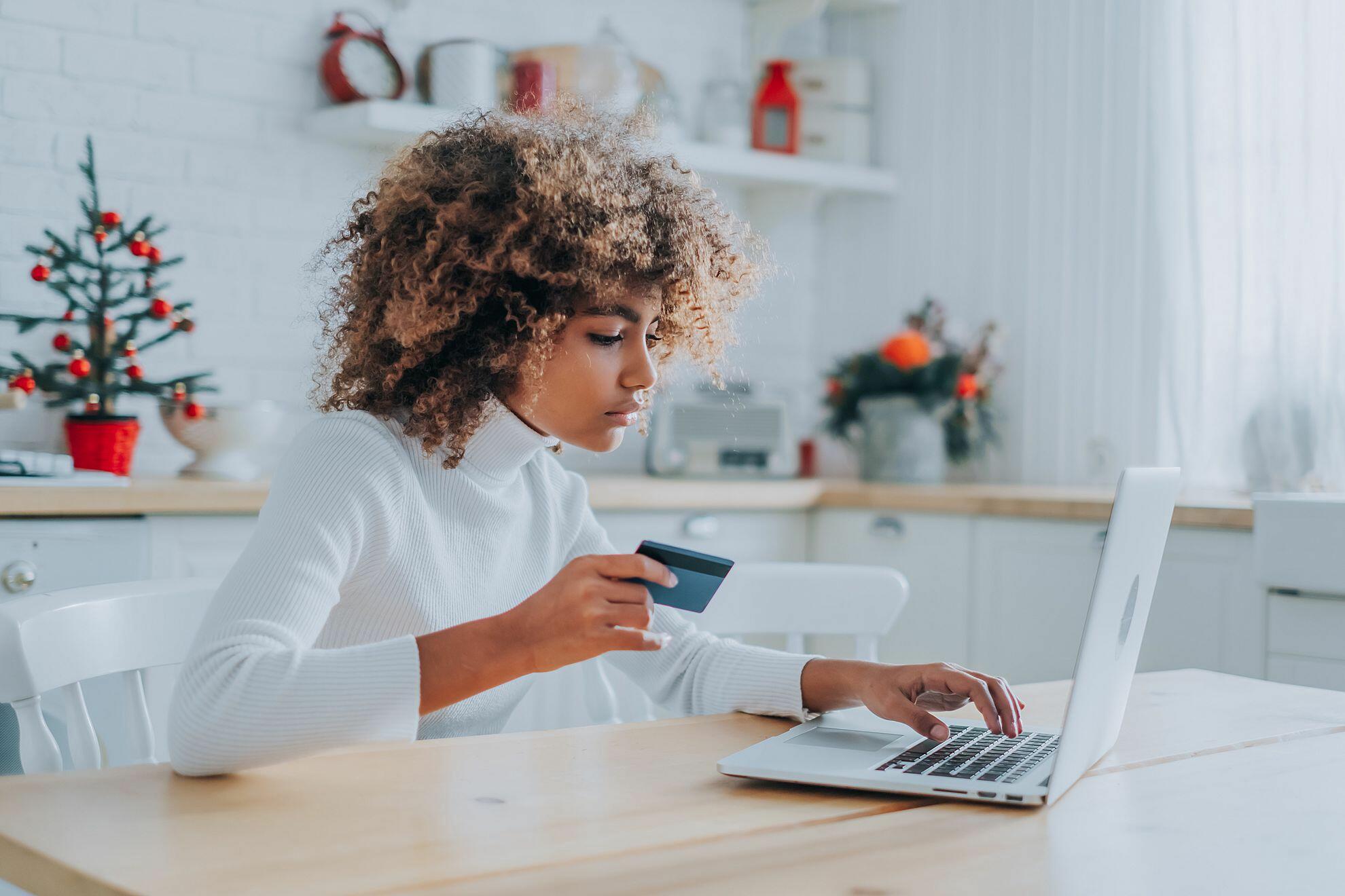 Mulher sentada em uma cadeira, segurando um cartão, mexendo no computador a mesa, vendo sua fatura Credz