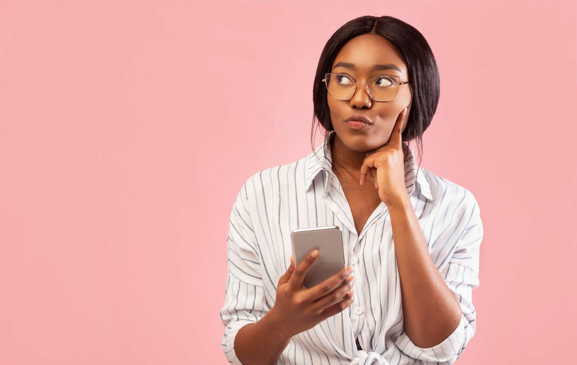 Mulher segurando o celular e com dúvidas sobre a fatura do cartão