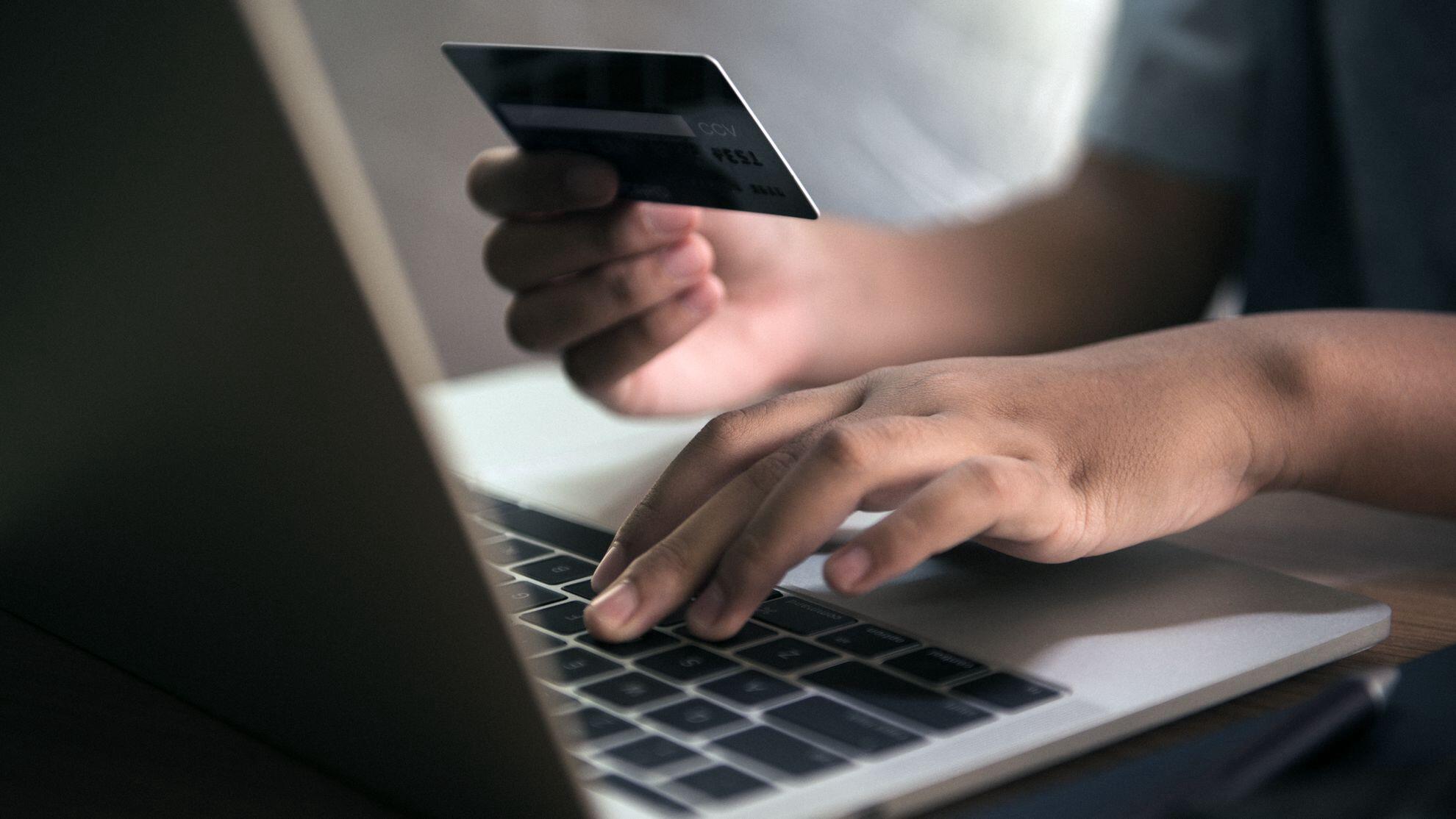 mãos masculinas teclando um notebook e segurando um cartão de débito